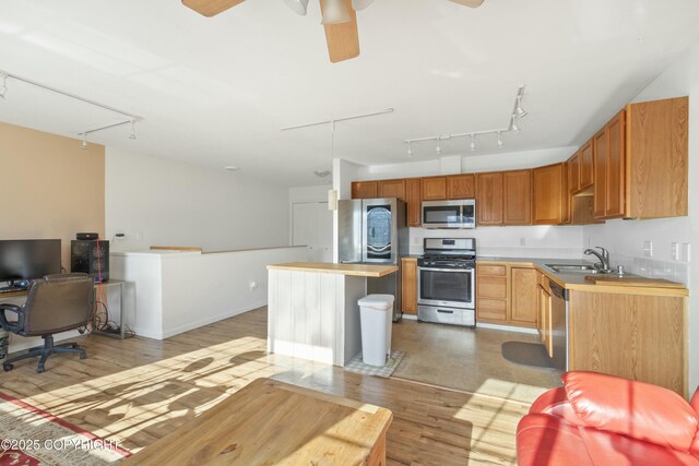 kitchen featuring light wood finished floors, stainless steel appliances, a kitchen island, a ceiling fan, and a sink