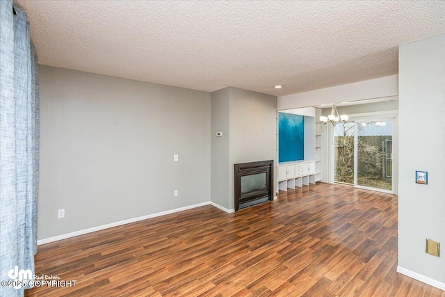 unfurnished living room with a textured ceiling, wood finished floors, baseboards, a chandelier, and a glass covered fireplace