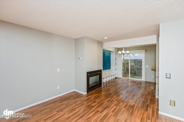 unfurnished living room with a glass covered fireplace, wood finished floors, baseboards, a textured ceiling, and a chandelier