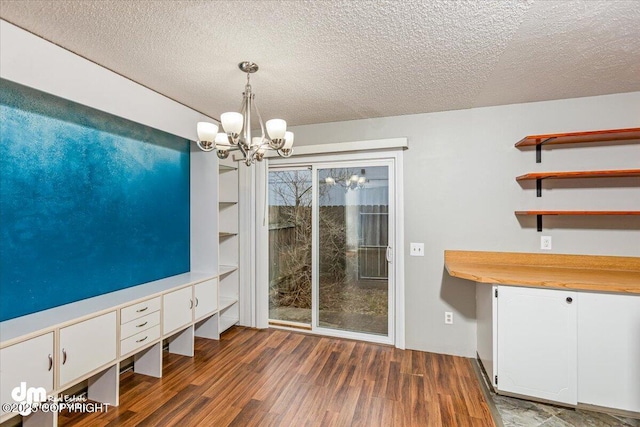 unfurnished dining area with a textured ceiling, dark wood finished floors, and a notable chandelier