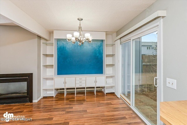 unfurnished dining area with a fireplace, a textured ceiling, a chandelier, built in shelves, and wood finished floors