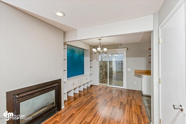 unfurnished dining area with a textured ceiling, a glass covered fireplace, wood finished floors, and a notable chandelier