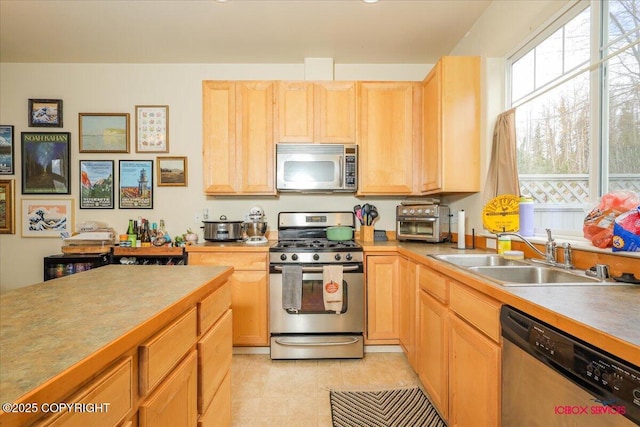 kitchen with appliances with stainless steel finishes, a sink, light brown cabinetry, and light countertops
