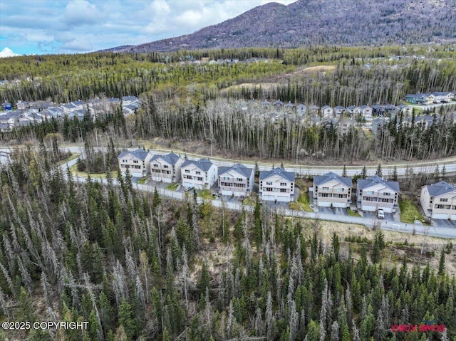 aerial view of property's location with a forest, nearby suburban area, and a mountainous background