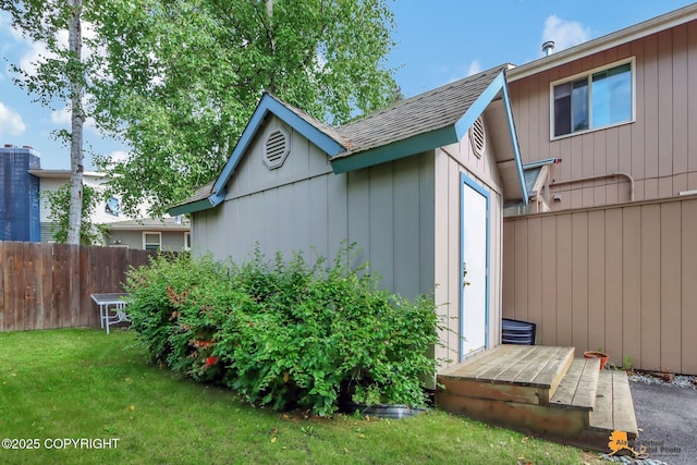 view of property exterior with a shingled roof, an outbuilding, fence, and a yard