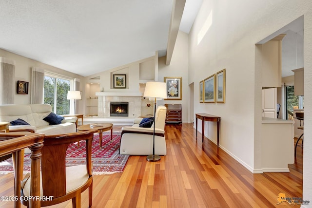 living room with baseboards, vaulted ceiling, a tiled fireplace, and light wood-type flooring