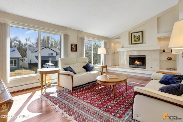 living room with light wood-type flooring, a baseboard heating unit, a tiled fireplace, and vaulted ceiling