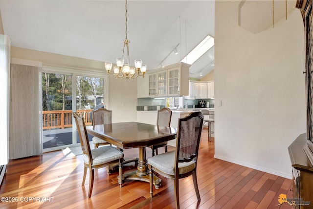 dining space featuring vaulted ceiling, rail lighting, light wood-type flooring, baseboards, and an inviting chandelier