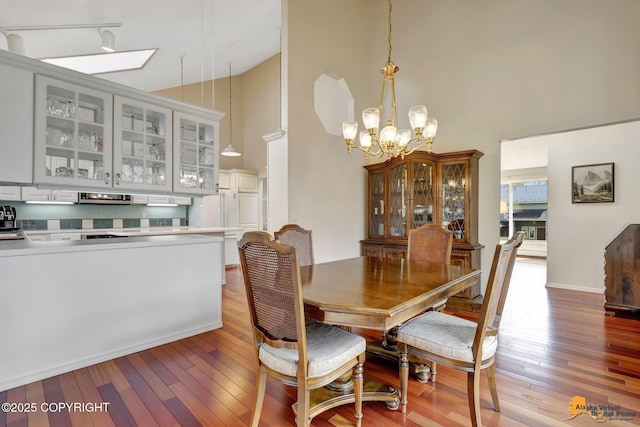 dining space with hardwood / wood-style floors, a skylight, a notable chandelier, and high vaulted ceiling