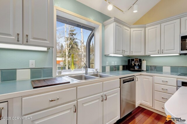 kitchen featuring white cabinets, track lighting, stainless steel appliances, dark wood-type flooring, and vaulted ceiling