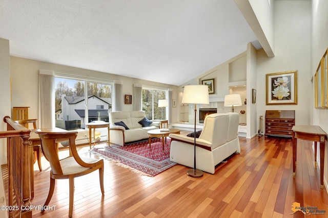 living room with high vaulted ceiling, a tiled fireplace, and light wood-type flooring