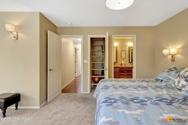 bedroom with baseboards, light colored carpet, and ensuite bath