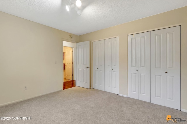 unfurnished bedroom with multiple closets, baseboards, carpet, and a textured ceiling