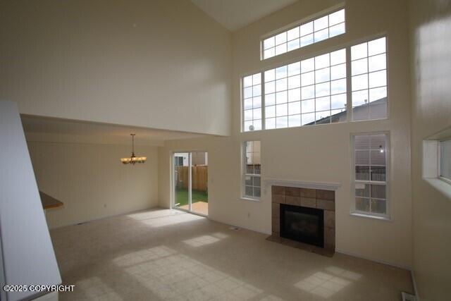 unfurnished living room featuring high vaulted ceiling, a chandelier, a fireplace, carpet flooring, and plenty of natural light