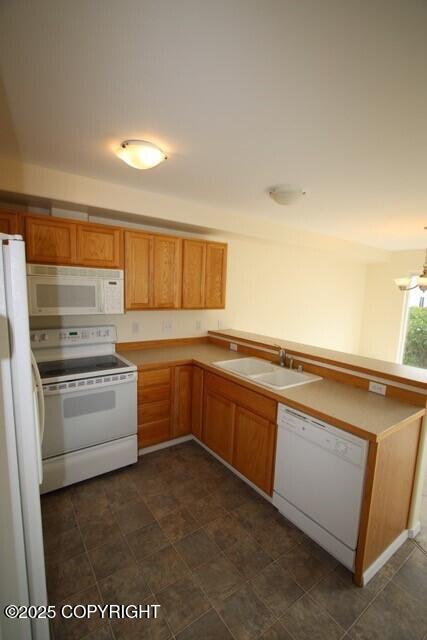 kitchen featuring white appliances, a sink, a peninsula, a chandelier, and brown cabinetry