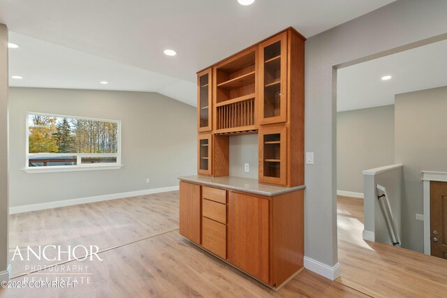 kitchen with glass insert cabinets, lofted ceiling, light wood finished floors, and brown cabinets