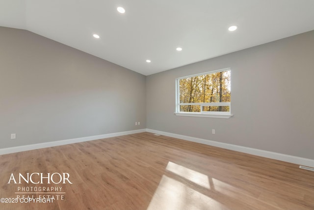 empty room featuring baseboards, vaulted ceiling, visible vents, and light wood-type flooring