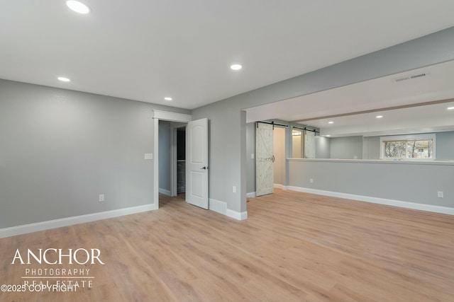 basement featuring baseboards, a barn door, light wood finished floors, and visible vents