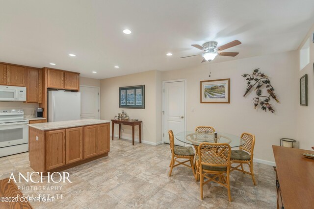 kitchen with light countertops, white appliances, a center island, baseboards, and a ceiling fan