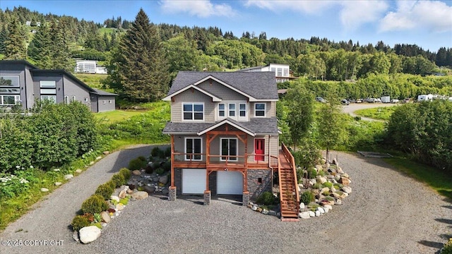 3866 Cabana Ct, Homer, AK 99603 - view of front of home featuring stairs, gravel driveway, a wooded view, an attached garage, and stone siding