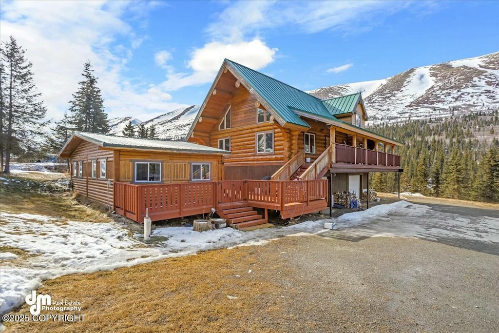 snow covered house featuring a deck with mountain view, metal roof, and log exterior