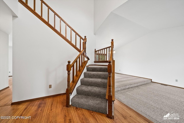 stairs with wood finished floors, vaulted ceiling, and baseboards