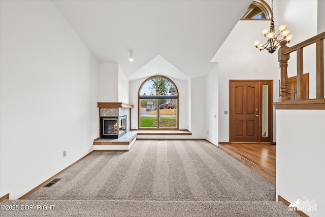 unfurnished living room with a glass covered fireplace, high vaulted ceiling, a chandelier, carpet, and wood finished floors