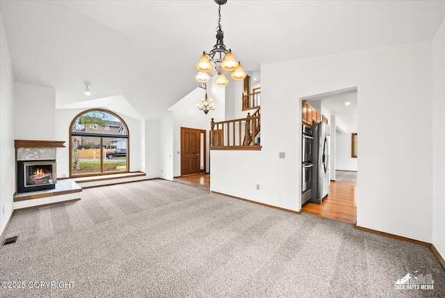 unfurnished living room featuring light carpet, a chandelier, baseboards, a glass covered fireplace, and high vaulted ceiling