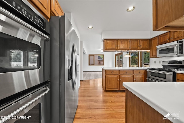 kitchen featuring stainless steel appliances, brown cabinets, recessed lighting, light wood-type flooring, and a peninsula