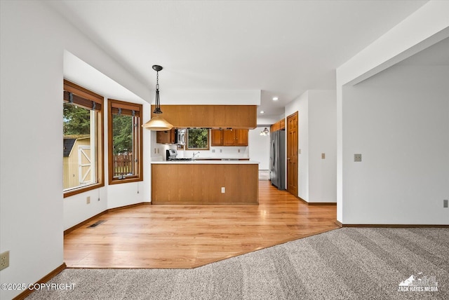 kitchen with freestanding refrigerator, a peninsula, brown cabinets, light carpet, and recessed lighting