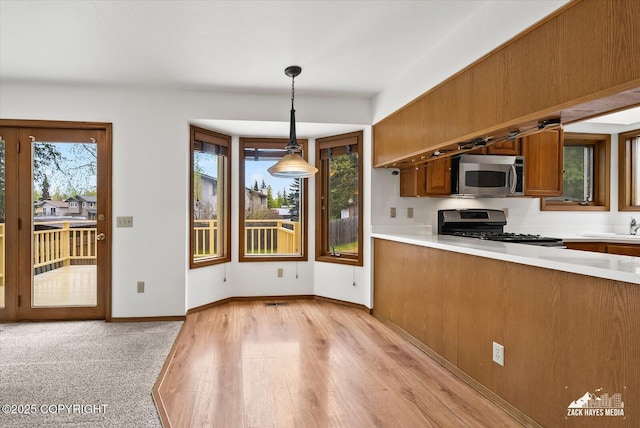 kitchen featuring stainless steel appliances, brown cabinets, light countertops, light wood finished floors, and decorative light fixtures