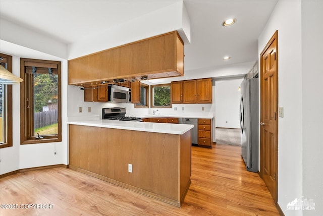 kitchen featuring appliances with stainless steel finishes, a sink, a peninsula, light wood-style floors, and brown cabinets