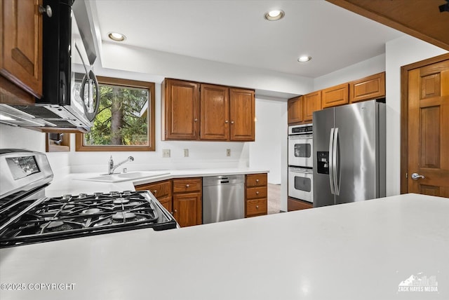 kitchen with stainless steel appliances, a sink, light countertops, recessed lighting, and brown cabinetry