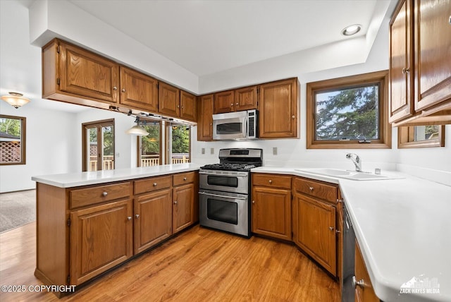 kitchen featuring stainless steel appliances, a sink, a peninsula, light countertops, and brown cabinetry