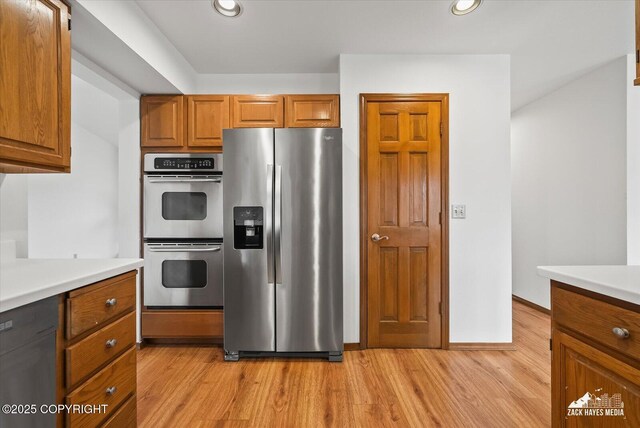 kitchen with stainless steel appliances, brown cabinets, light wood-style flooring, recessed lighting, and light countertops