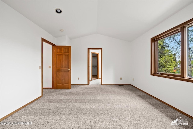 unfurnished bedroom featuring vaulted ceiling, baseboards, light colored carpet, and a walk in closet