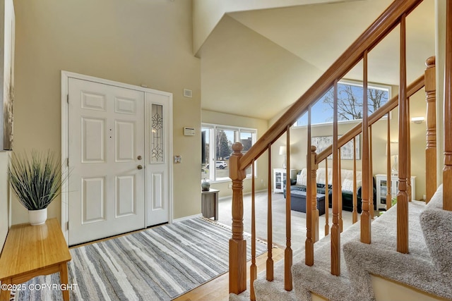 carpeted entryway featuring a towering ceiling, stairs, and baseboards