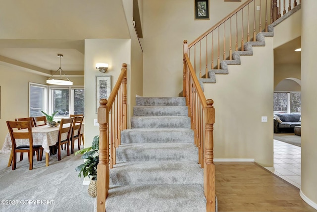 stairs with arched walkways, wood finished floors, a high ceiling, and baseboards