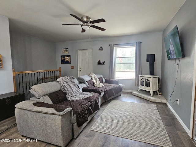 bedroom featuring a wood stove, dark wood-style floors, a ceiling fan, and baseboards