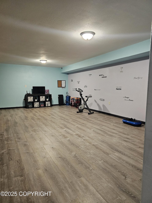 exercise area featuring wood finished floors, a textured ceiling, and baseboards