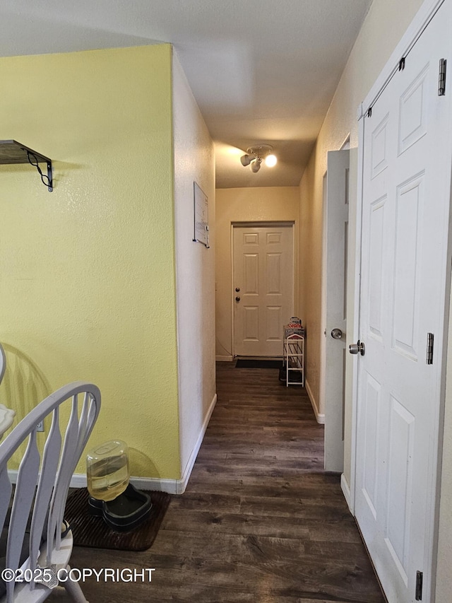 corridor with dark wood finished floors, baseboards, and a textured wall