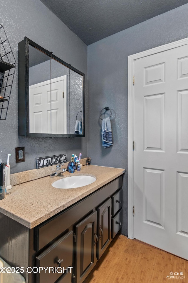 bathroom featuring vanity, a textured wall, a textured ceiling, and wood finished floors
