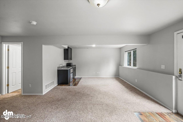 unfurnished living room featuring a sink, baseboards, light colored carpet, and visible vents