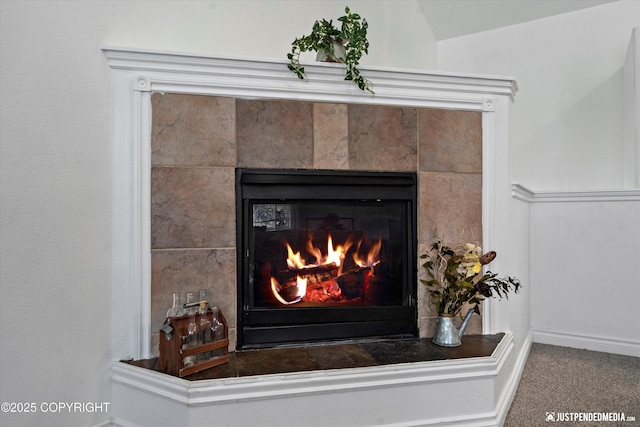 interior details with a tiled fireplace, baseboards, and carpet flooring