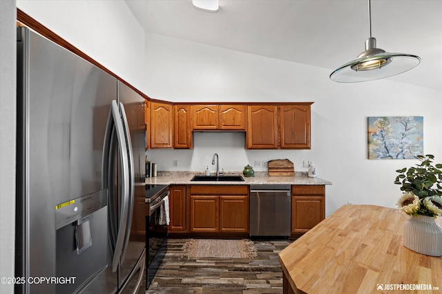 kitchen featuring appliances with stainless steel finishes, dark wood-type flooring, brown cabinetry, lofted ceiling, and a sink