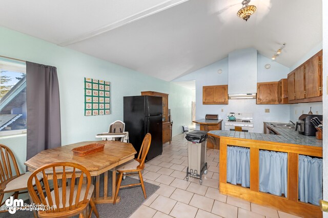 65265 Knob Hill Rd, Anchor Point, AK 99556 - kitchen with light tile patterned floors, freestanding refrigerator, brown cabinetry, white range with gas stovetop, and lofted ceiling