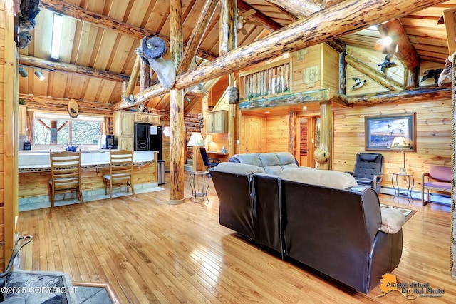 living room featuring light wood-type flooring, high vaulted ceiling, beamed ceiling, and wooden walls