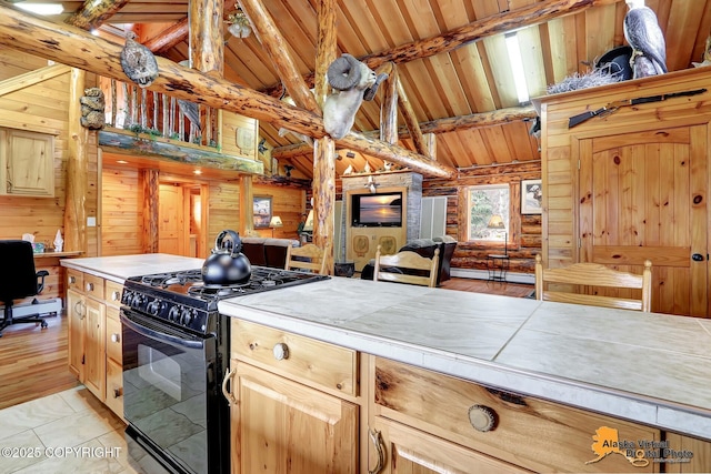 kitchen featuring tile countertops, wooden ceiling, black gas stove, wooden walls, and beam ceiling