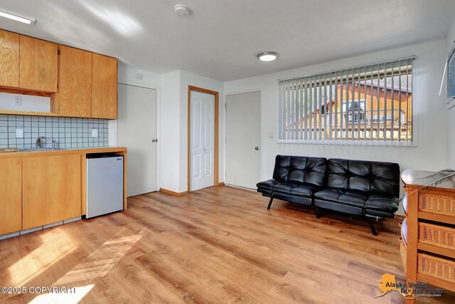 kitchen with light wood-type flooring, tile counters, backsplash, fridge, and a sink