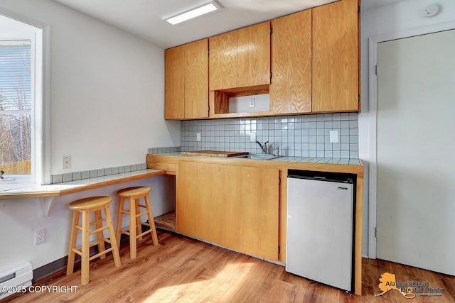 kitchen with backsplash, tile countertops, a sink, a baseboard radiator, and fridge